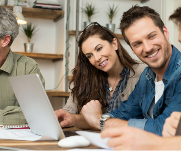 group of people in a meeting table with lots on it, the lady is smiling looking at the laptop monitor